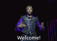 a man wearing a purple shirt and a crown is standing on a stage with his arms outstretched and says welcome