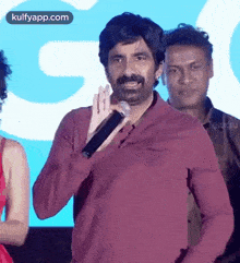 a man with a mustache is holding a microphone in his hand and talking into it .