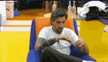 a man in a white shirt is sitting in a chair with his legs crossed