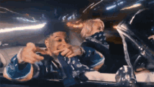 a man and a woman are sitting in a car and the man is pointing at the camera .