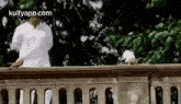 a man in a white shirt is standing on a balcony next to a bird .