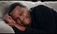 a man is crying while laying on a couch with his eyes closed .