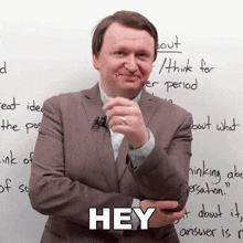 a man in a suit stands in front of a white board with the word hey on it