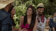 a woman in a pink dress is surrounded by a group of people wearing hats
