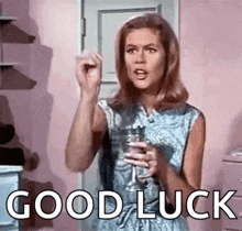 a woman is holding a glass of wine and saying `` good luck '' while standing in a room .