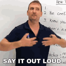 a man is standing in front of a white board with the words say it out loud written on it