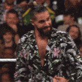 a man with a beard wearing a floral jacket is standing in front of a crowd .
