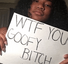 a woman holds a sign that says wtf you goofy bitch
