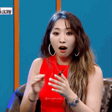 a woman wearing a red tank top and hoop earrings is sitting on a couch