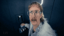 a man wearing glasses and a fur coat is standing in front of a keypad that says lw on it