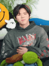 a man in a hoodie is sitting on a couch holding a stuffed turtle .