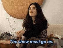 a woman sits in a chair with the words " the show must go on " written below her