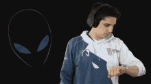 a man wearing headphones looks at his watch in front of an alien