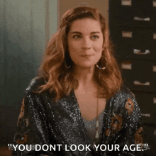 a woman in a sequined jacket is making a funny face and says `` you don 't look your age '' .
