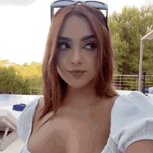 a woman wearing sunglasses and a white top is taking a selfie by a pool .
