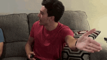 a man in a red shirt is sitting on a couch holding a remote control