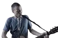 a man in a blue shirt is singing into a microphone while playing a guitar