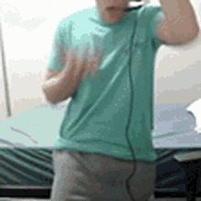 a man in a green t-shirt is standing in front of a bed .