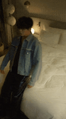a man in a blue denim jacket is standing on a bed