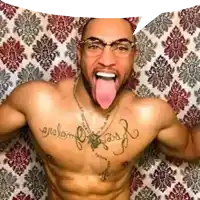 a shirtless man with glasses and tattoos on his chest is sticking his tongue out .