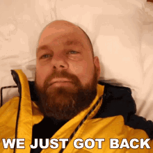 a bald man with a beard is laying on a bed with the words " we just got back " above him