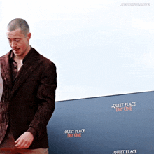 a man in a brown jacket stands in front of a wall that says quiet place day one