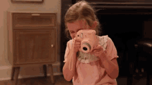 a little girl is taking a picture with a pink camera
