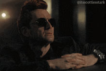 a man wearing sunglasses says " alright " while sitting at a table