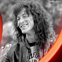 a black and white photo of a smiling man with long curly hair