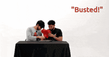 two men are sitting at a table with the words " busted " on the bottom