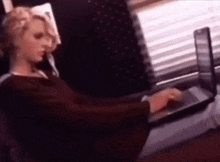 a woman is typing on a laptop computer while sitting in front of a window .