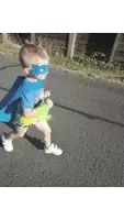 a young boy wearing a blue cape and mask is running on a road