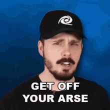 a man with a beard is wearing a baseball cap and a black shirt and says `` get off your arse '' .