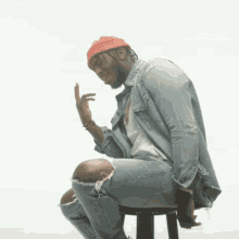 a man sitting on a stool wearing a red beanie and ripped jeans