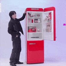 a man is standing in front of a red refrigerator that has the door open