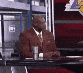 a man in a suit and tie is sitting at a desk in front of a lakers logo