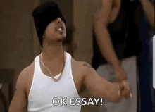 a man wearing a white tank top and a black hat is giving a thumbs up and saying `` ok essay '' .