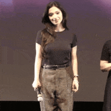 a woman in a black shirt and plaid pants is holding a microphone and smiling