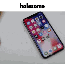 a cell phone with a cracked screen is sitting on a table with the words holesome above it .