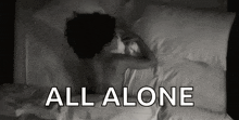 a woman is laying on a bed with the words all alone above her .