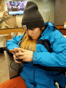 a woman wearing a carhartt hat and a blue jacket looks at her phone