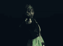 a woman in a green dress is holding a gun in her right hand