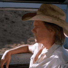 a man wearing a cowboy hat and a white shirt is leaning out of a window