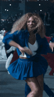 a woman with curly hair is dancing in a blue outfit