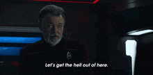a man with a beard is standing in a dark room and says let 's get the hell out of here .