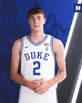 a duke basketball player stands with his hands folded in front of a blue background